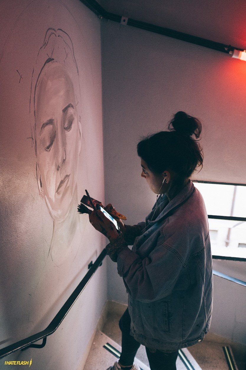 Artista trabalhando em uma parede, em registro do Café Preto
